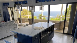 A modern kitchen with a large island, built-in oven, and a view of the ocean through large windows.