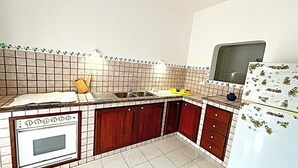 Cocina compacta con salpicadero de azulejos, un lavamanos, estufa y refrigerador.