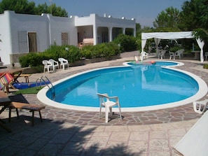 Une piscine avec une zone bordée de blanc, des chaises longues et un espace de repos abrité.