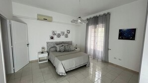 Un dormitorio con cama, mesitas de noche, ventilador de techo, aire acondicionado de pared y un cuadro en la pared.