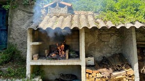 Eine rustikale Gartenlaube mit Ziegeldach, einem Feuer im Inneren und einem Holzstapel davor.