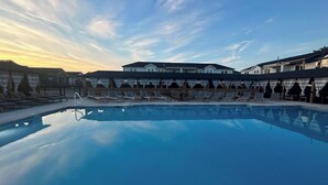 A swimming pool with lounge chairs and umbrellas, surrounded by buildings with a modern architectural style. - CHIll IN! Central to Everything! Steps to Beach! (Corolla)