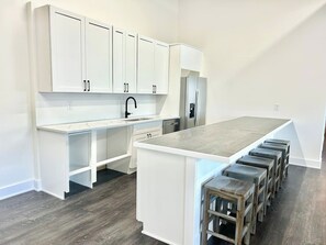 Une cuisine moderne avec des meubles blancs, un îlot central doté de tabourets et un lave-vaisselle encastré.