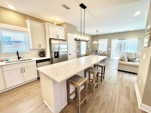 A modern kitchen with white cabinetry, a large island, and a dining area with wooden stools.