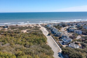 Vue aérienne d’une zone résidentielle côtière, avec des maisons, une plage et une route.