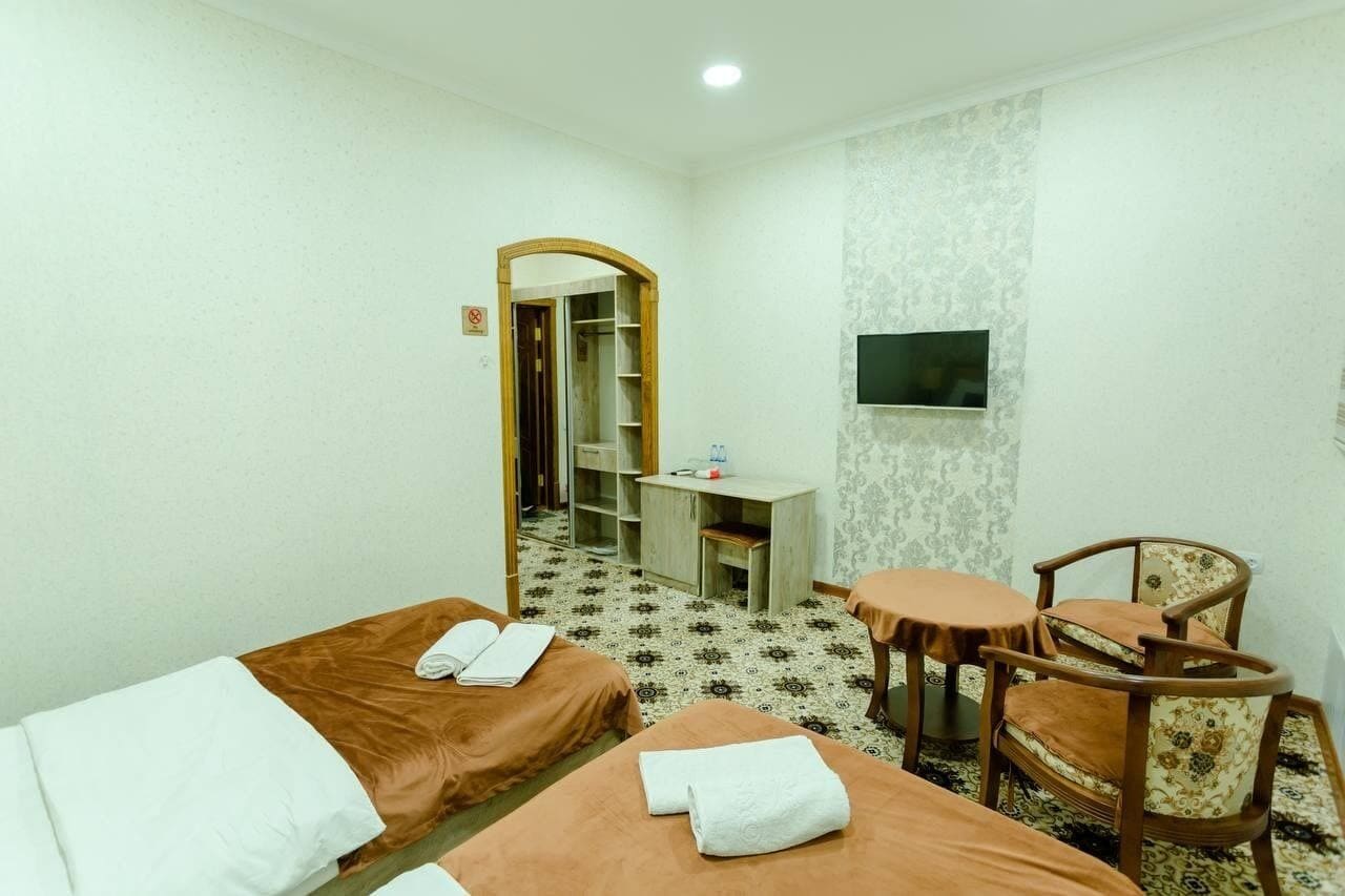A hotel room with two beds, a desk, a chair, and a TV.