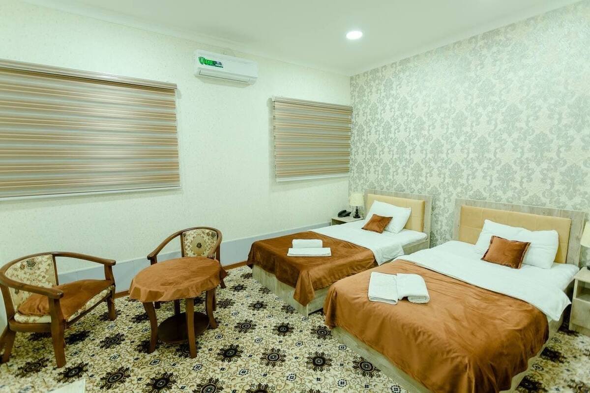 A hotel room with two single beds, a small table, two chairs, and a patterned floor.