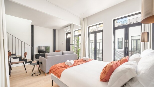 Moderni hotellihuone, jossa on suuri sänky, sohva, televisio ja parveke, jolta on näkymä.