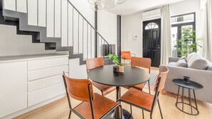Moderni olohuone, jossa on portaikko, ruokailutila pyöreällä pöydällä ja tuoleilla, sohva ja pieni sivupöytä.