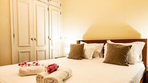 A neatly made bed with pillows and a rolled towel, a wooden headboard, and a white wardrobe with multiple doors. - GuestReady - Family-Friendly Haven in Funchal (Funchal)