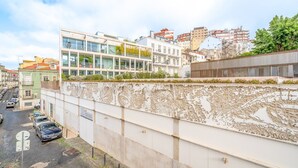 Un edificio moderno con fachada de vidrio, junto a edificios más antiguos con balcones.