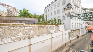 Una calle con un edificio blanco que presenta un mural grande en su fachada, adoquinada y con un coche estacionado.