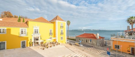 A coastal town with yellow buildings, a paved area with outdoor seating, and a view of the sea.