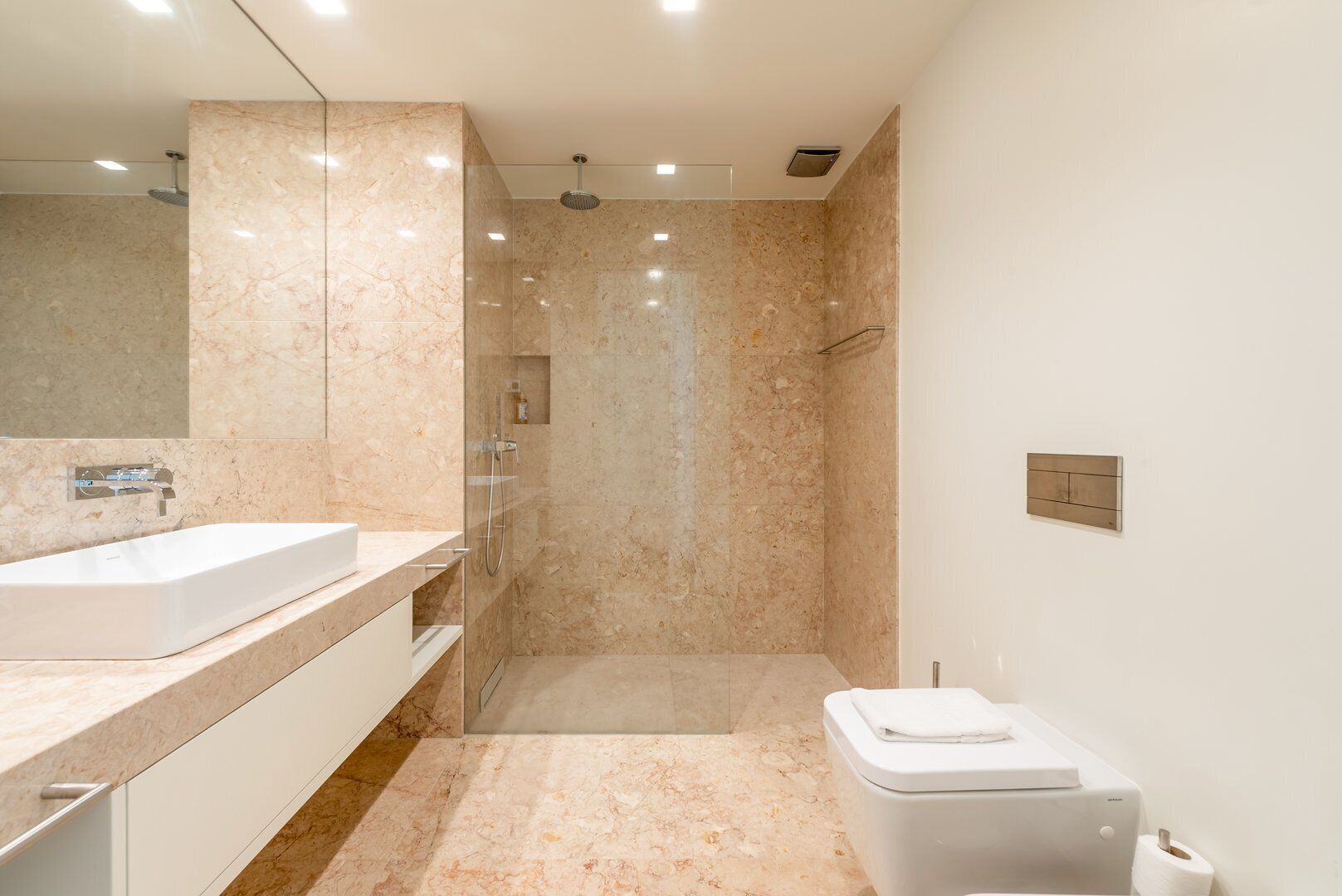 A modern bathroom with a large mirror, a sink, a shower, and a toilet.