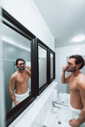 A man in a bathroom with a large mirror, white tiles, and a white sink.