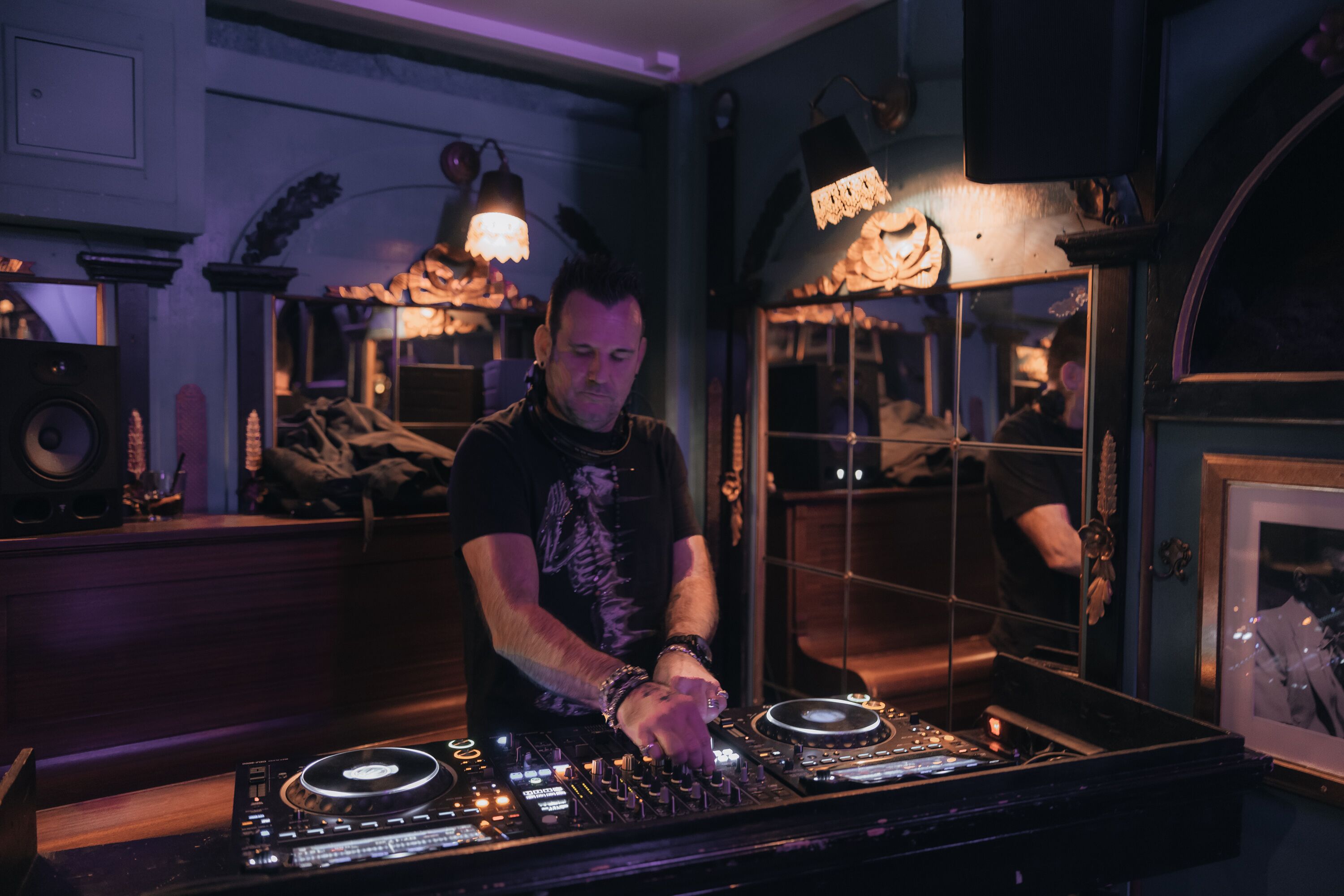 Een DJ-kraam met een draaitafel en mengpaneel, omringd door speakers en een spiegel.