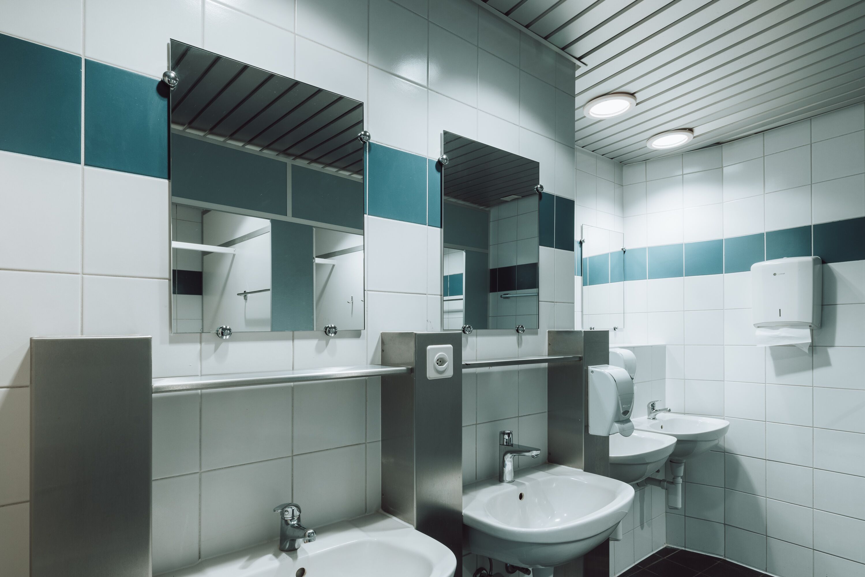A modern bathroom with two sinks, a mirror, and a hand dryer.