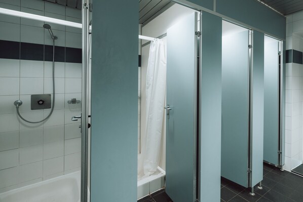 Baño público con ducha, cabinas de inodoros y secamanos.