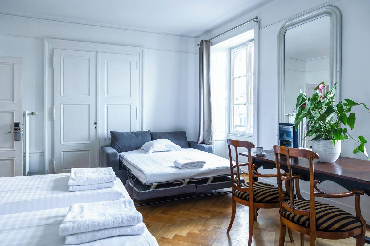 Habitación de hotel con cama, escritorio con silla, planta en maceta y un espejo grande.