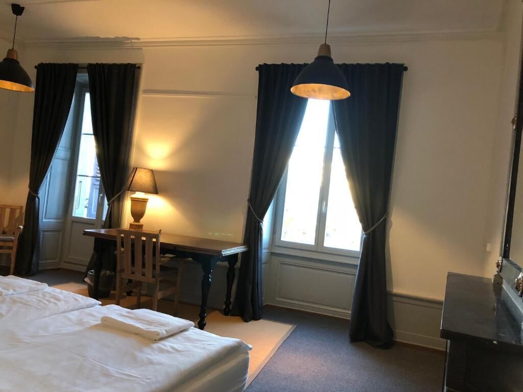 A hotel room with a bed, a desk, a chair, a lamp, and a window with curtains.