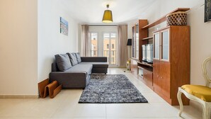 Una sala de estar moderna con un sofá seccional gris, un tapete blanco y negro, un mueble de madera con un televisor y una silla amarilla.