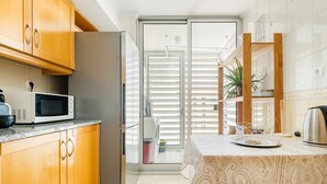 Una cocina compacta con armarios de madera, microondas, refrigerador y una mesa con mantel estampado.