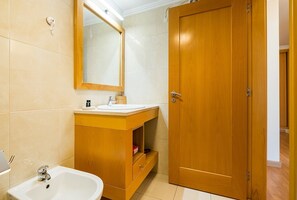 Bathroom features a bathtub, sink, and mirror, with a shelf for storage.