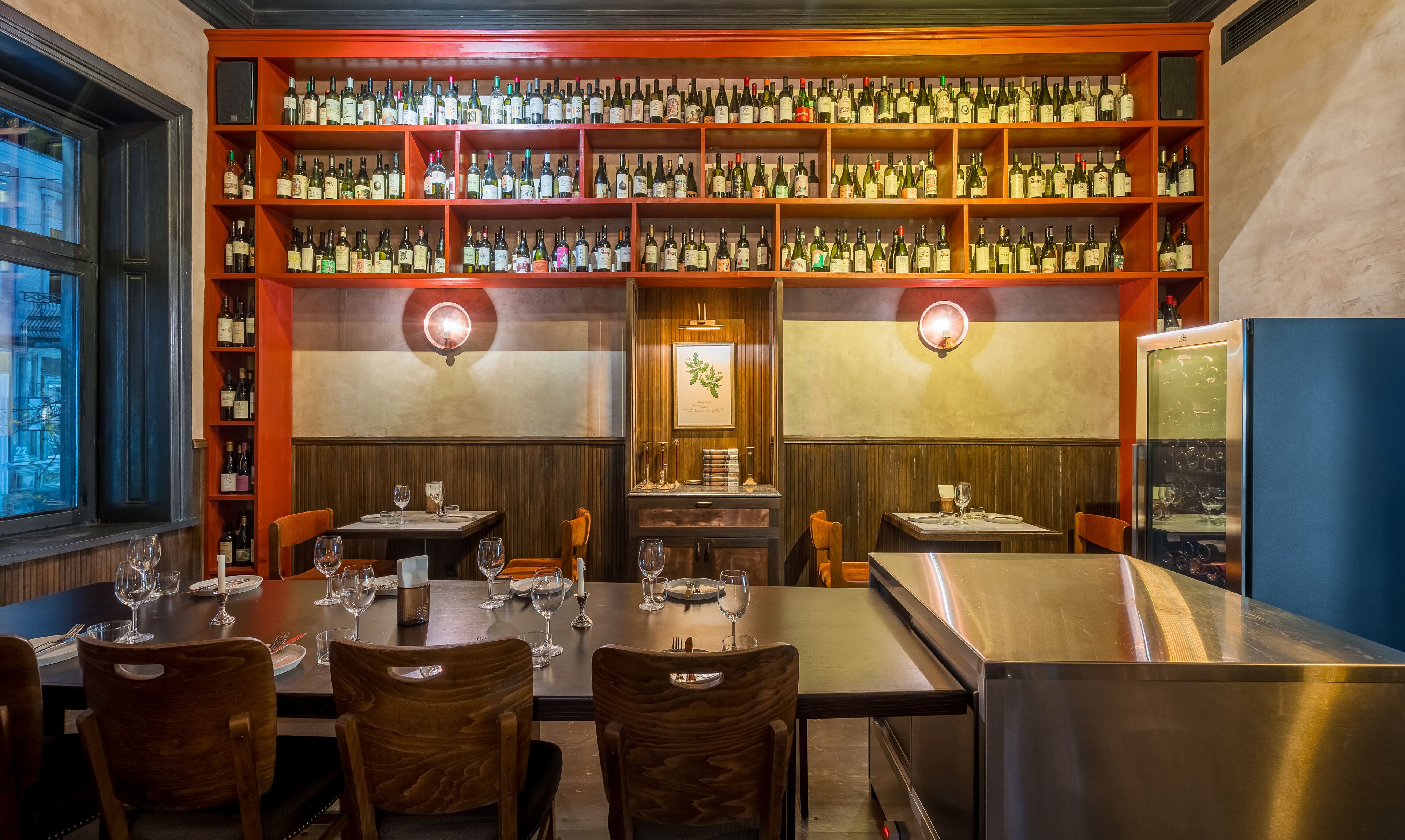 Un restaurante con varias mesas de comedor, cada una dispuesta con copas de vino y cubiertos. Las paredes están revestidas de estanterías llenas de botellas de vino.
