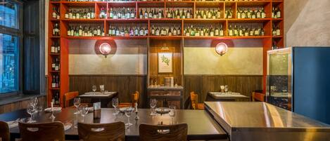 Un restaurante con varias mesas de comedor, cada una dispuesta con copas de vino y cubiertos. Las paredes están revestidas de estanterías llenas de botellas de vino.
