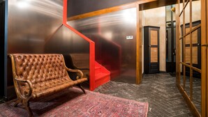 A room with a tufted leather bench, a red staircase, and a patterned rug. - Communal Hotel Kutaisi (Kutaisi)