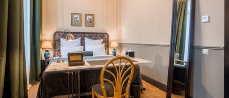 Habitación de hotel con cama, lámparas de noche, escritorio con silla, espejo y un cuadro de un ciervo en la pared.