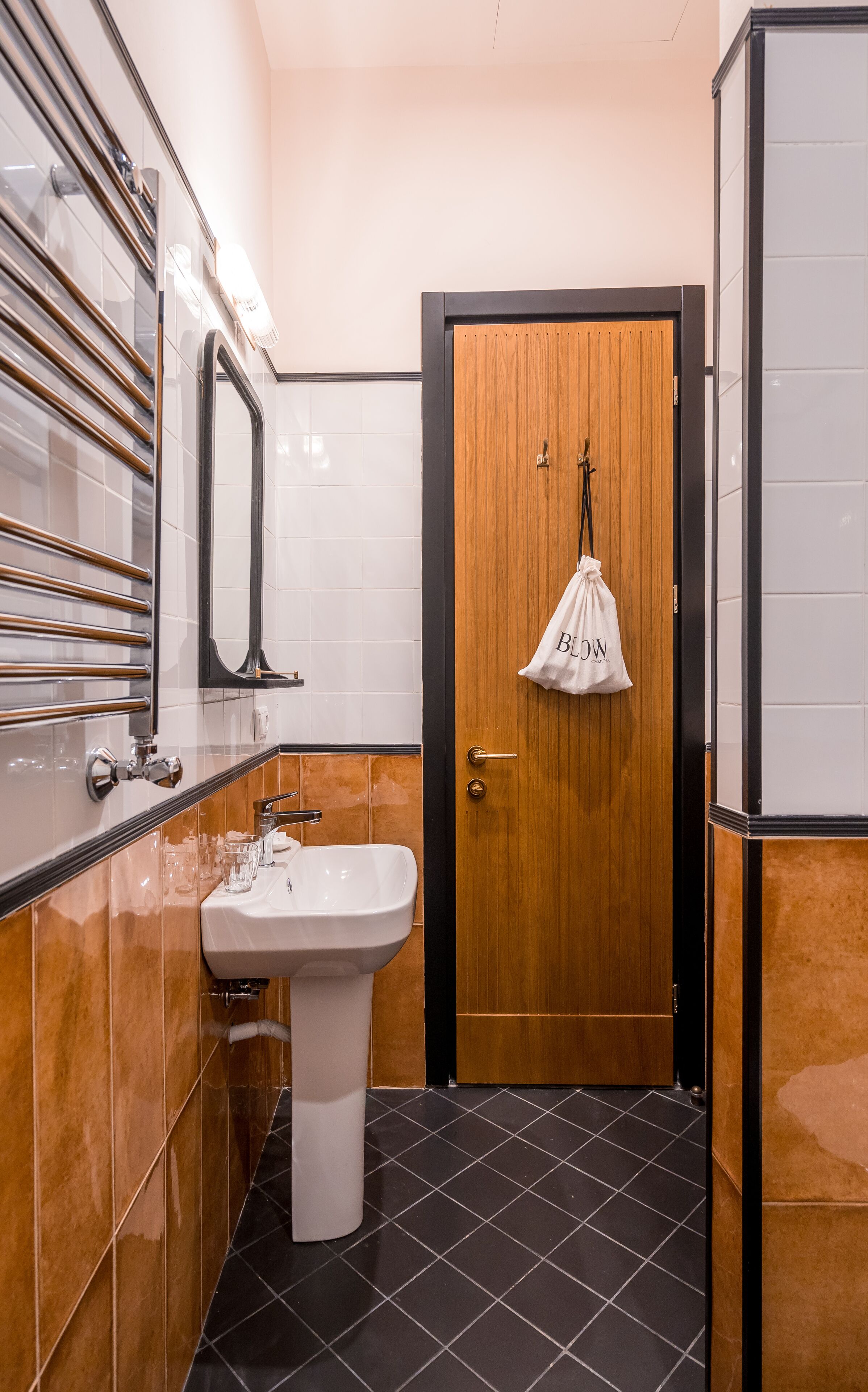 A bathroom with a white sink, a wooden door, and a towel hanging on the wall.