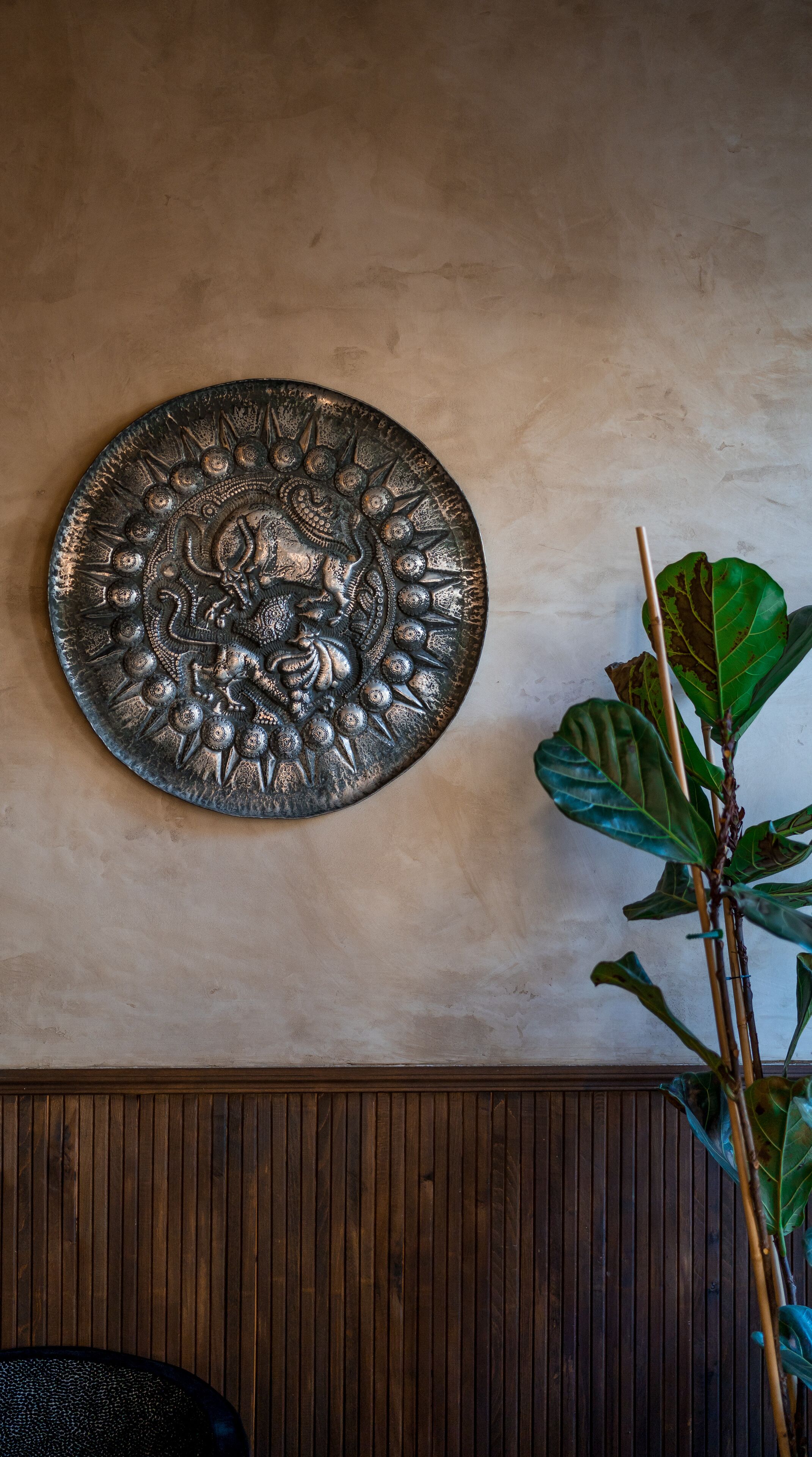 A wall with a decorative metal plate and a potted plant.
