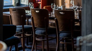 A restaurant with wooden chairs and tables, a wine rack with bottles, and a window with a view of buildings. - Communal Hotel Kutaisi (Kutaisi)