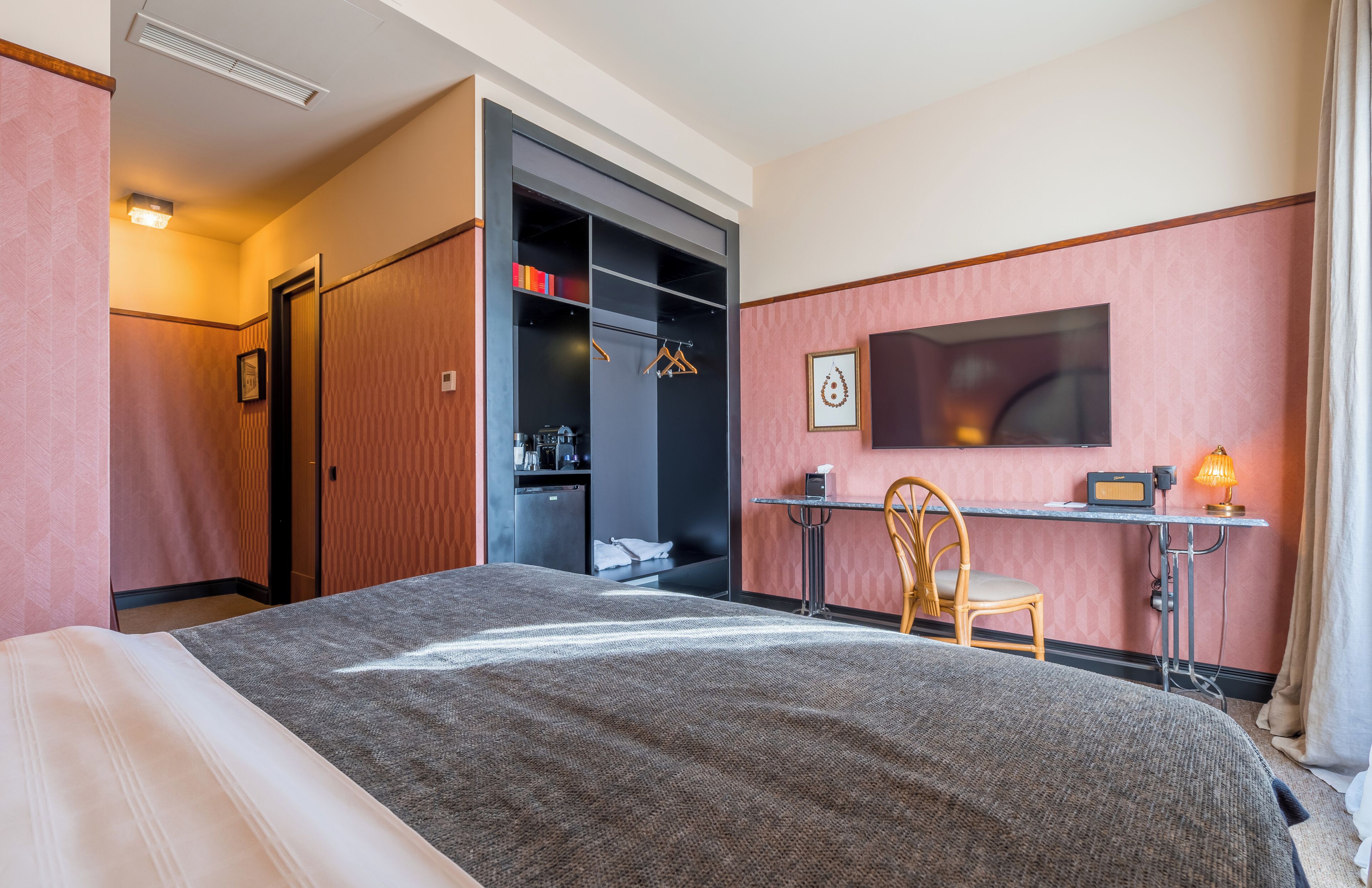 A hotel room with a bed, a desk with a chair, a wardrobe, and a TV.