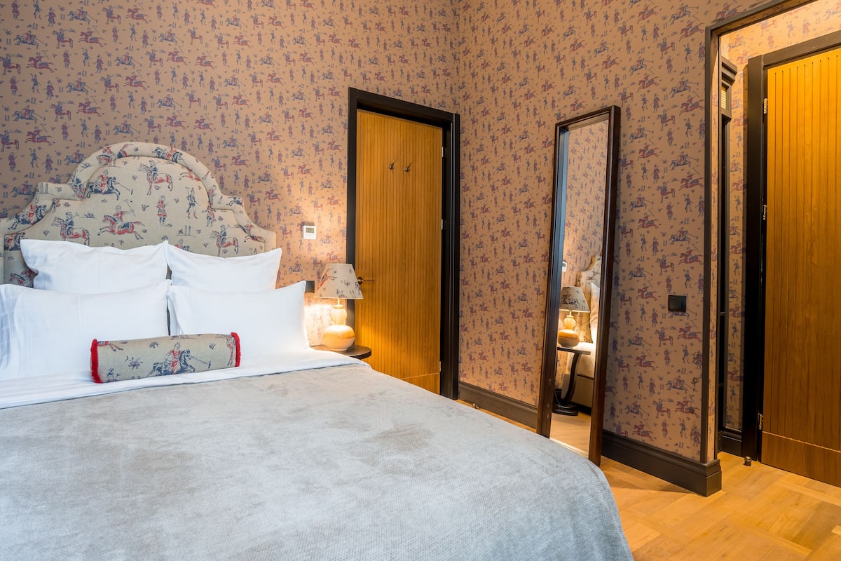A neatly made bed with white linens and a decorative pillow, a bedside lamp, and a wooden door with a mirror.