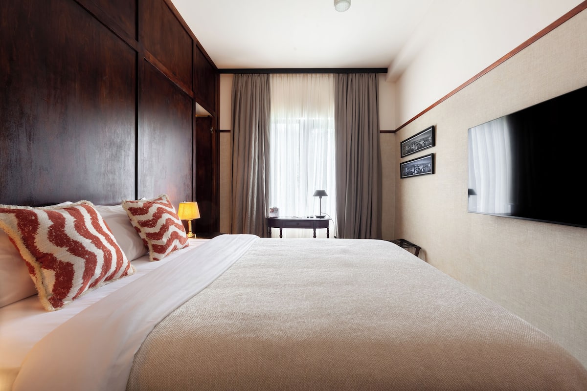 A hotel room with a large bed, a desk with a lamp, and a TV on the wall.