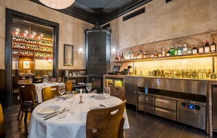 Een restaurant met gedekte tafels, een bar met flessen en een keuken op de achtergrond.
