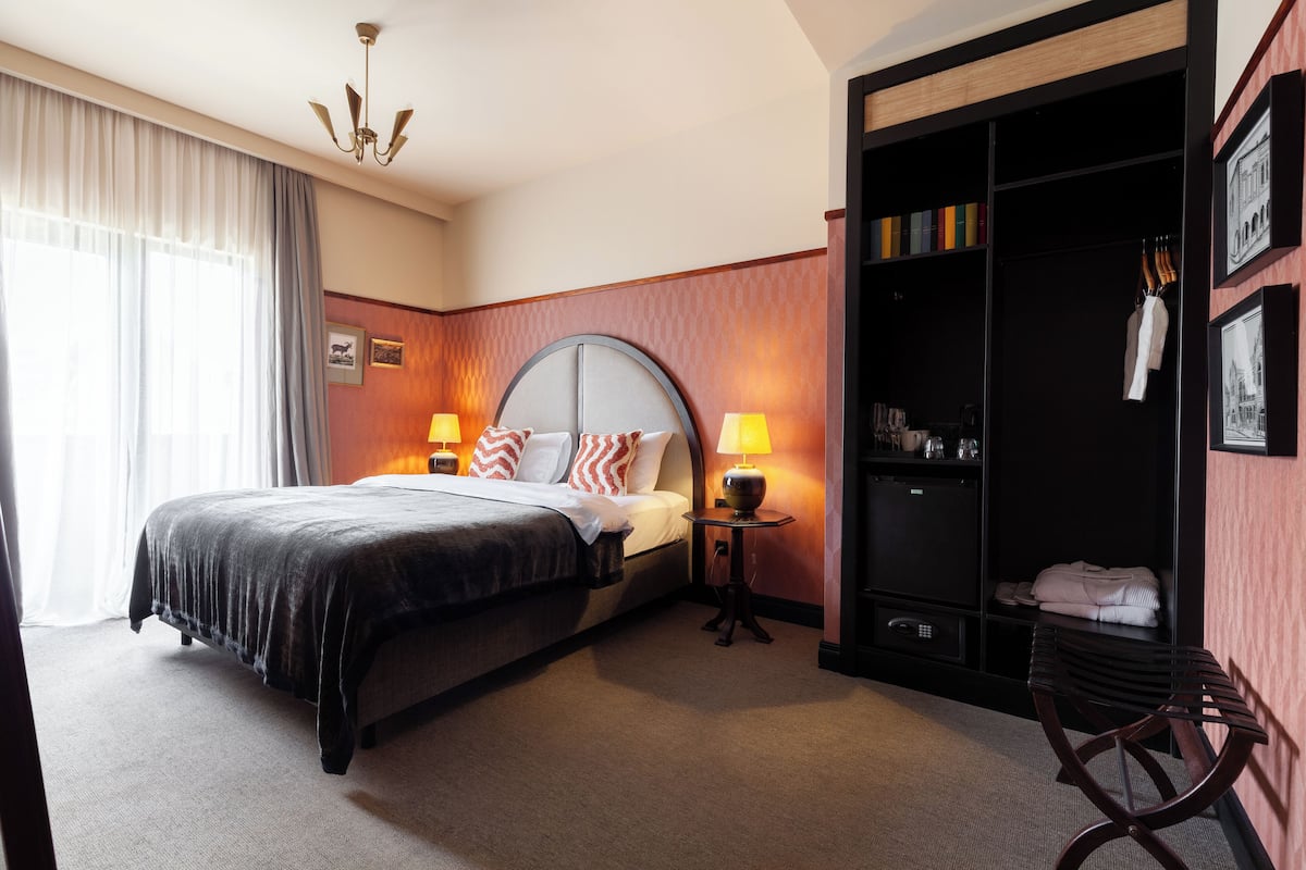A hotel room with a large bed, two bedside lamps, a wardrobe, and a bench.