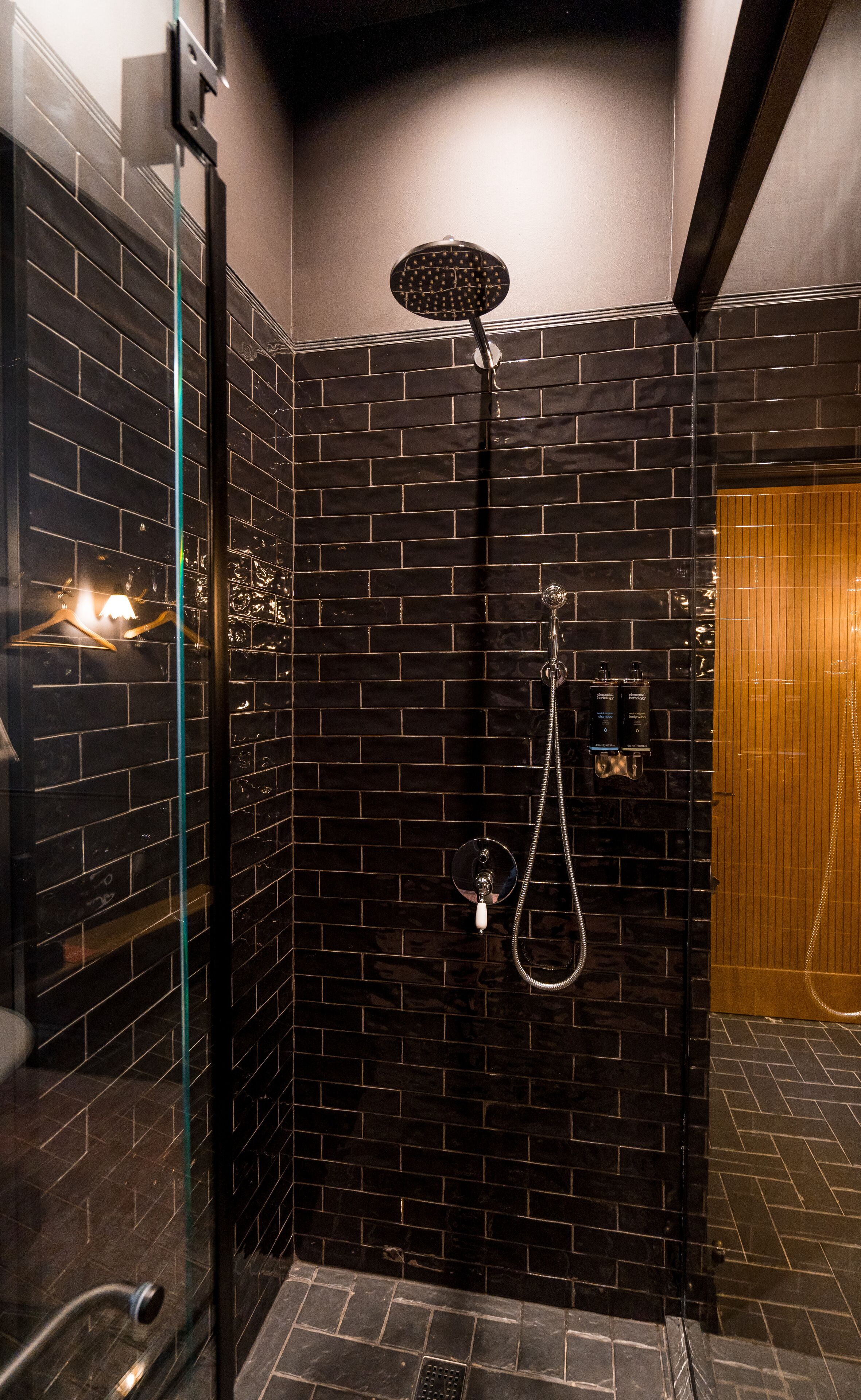 A bathroom with black tiled walls, a glass shower enclosure, and a wooden door.