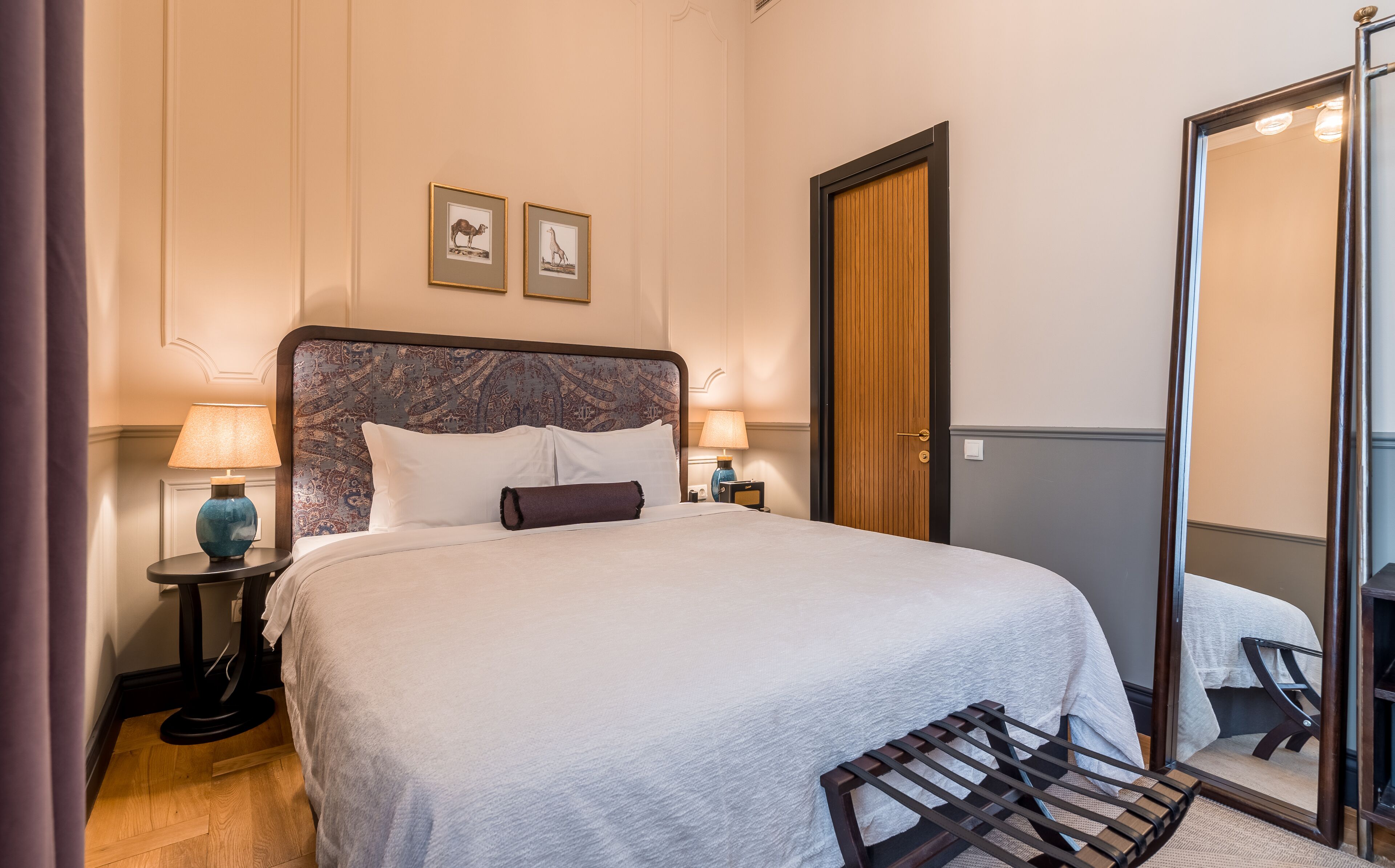 A neatly made bed with a headboard, two bedside lamps, a wooden door, and a mirror.