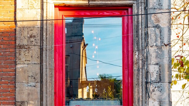 A red double door with a glass upper section, a brass door knocker, and a plaque reading "The COMMUNAL KUTAIJI". - Communal Hotel Kutaisi (Kutaisi)