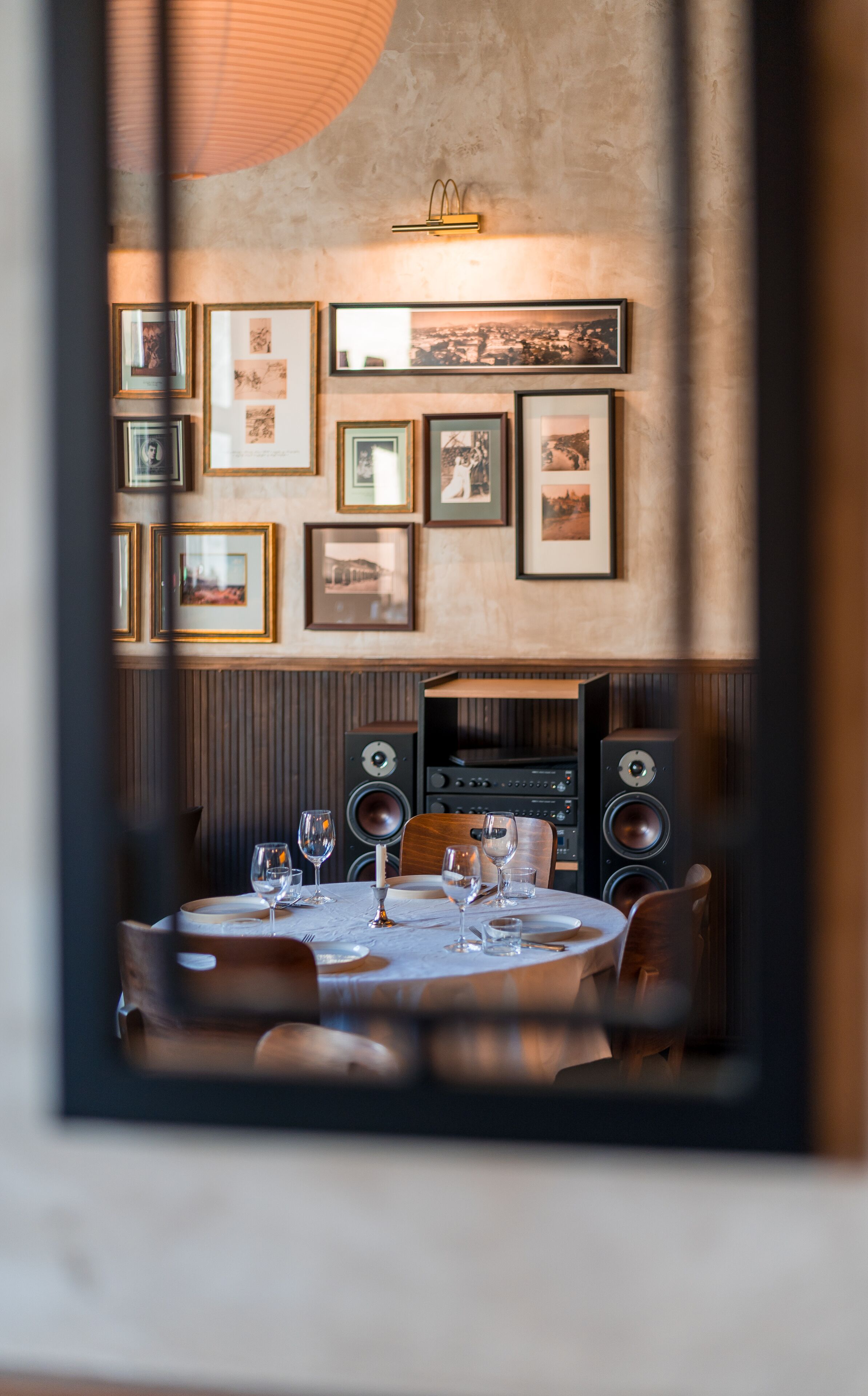 A dining area with a table set for two, framed pictures on the wall, and speakers in the background.