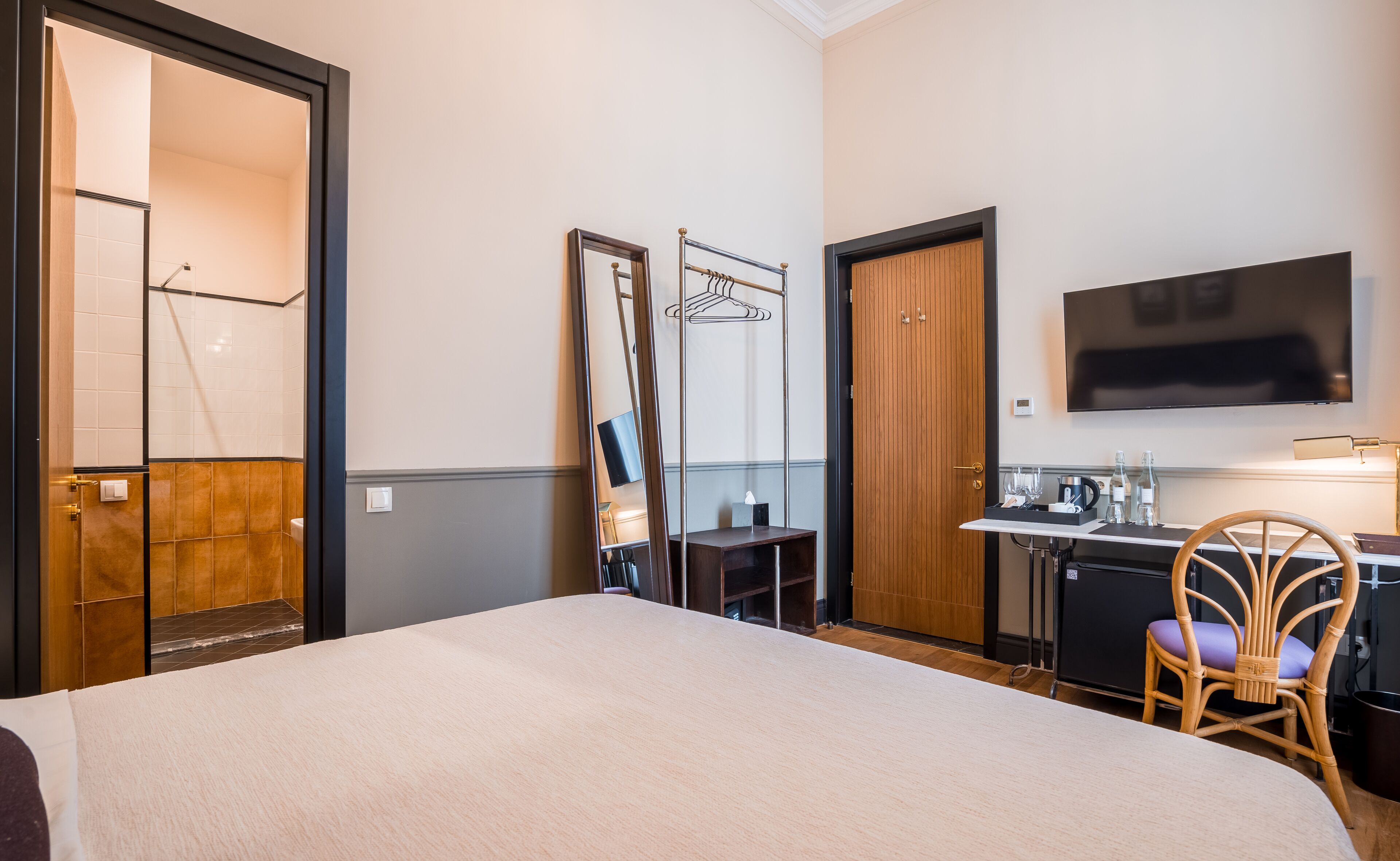 A hotel room with a large bed, a desk with a chair, a television, and a mirror.
