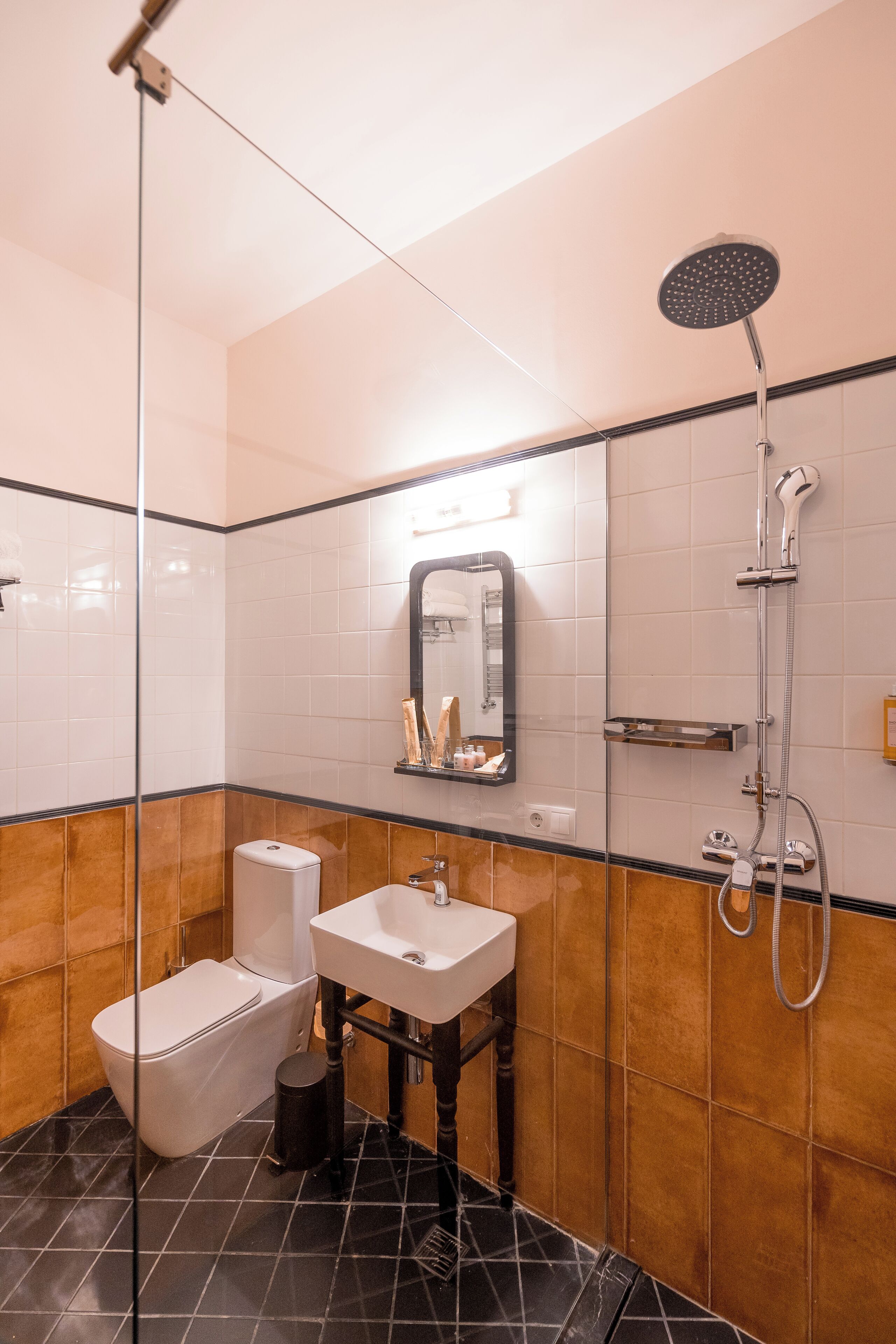A modern bathroom with a glass shower enclosure, a white toilet, a sink with a mirror above it, and a tiled floor.
