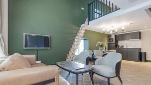 A modern living room with a sofa, a coffee table, and a TV mounted on the wall. There is a staircase leading to an upper level. - Bens The Walton (Amsterdam)