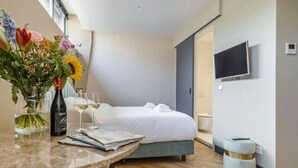 A hotel room with a bed, a TV mounted on the wall, a small round table with a vase of flowers, a bottle of wine, and glasses. - Bens The Walton (Amsterdam)