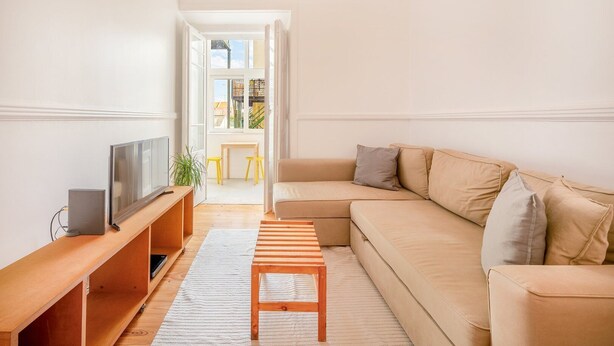 A modern living room with a beige sofa, a wooden coffee table, and a TV on a wooden stand.