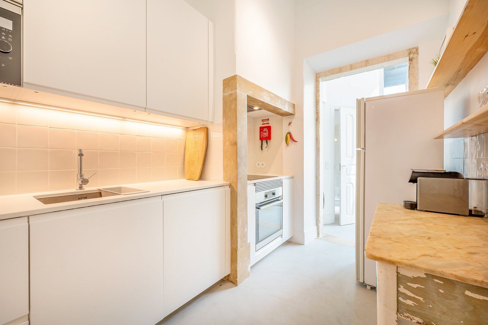 Una cocina moderna con armarios blancos, un lavamanos de acero inoxidable y un horno empotrado.