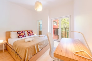 Enjoy a restful night's sleep in this serene bedroom with a comfortable bed, a large window offering a view of the balcony, and a convenient table and chair.